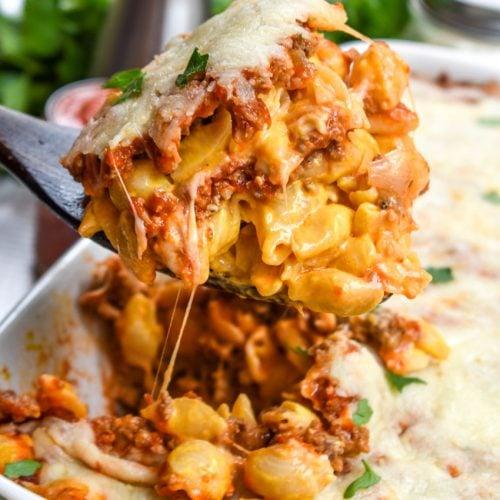 side view of lasagna mac and cheese being served from a baking dish, showing the layers of pasta, cheese, and sauce