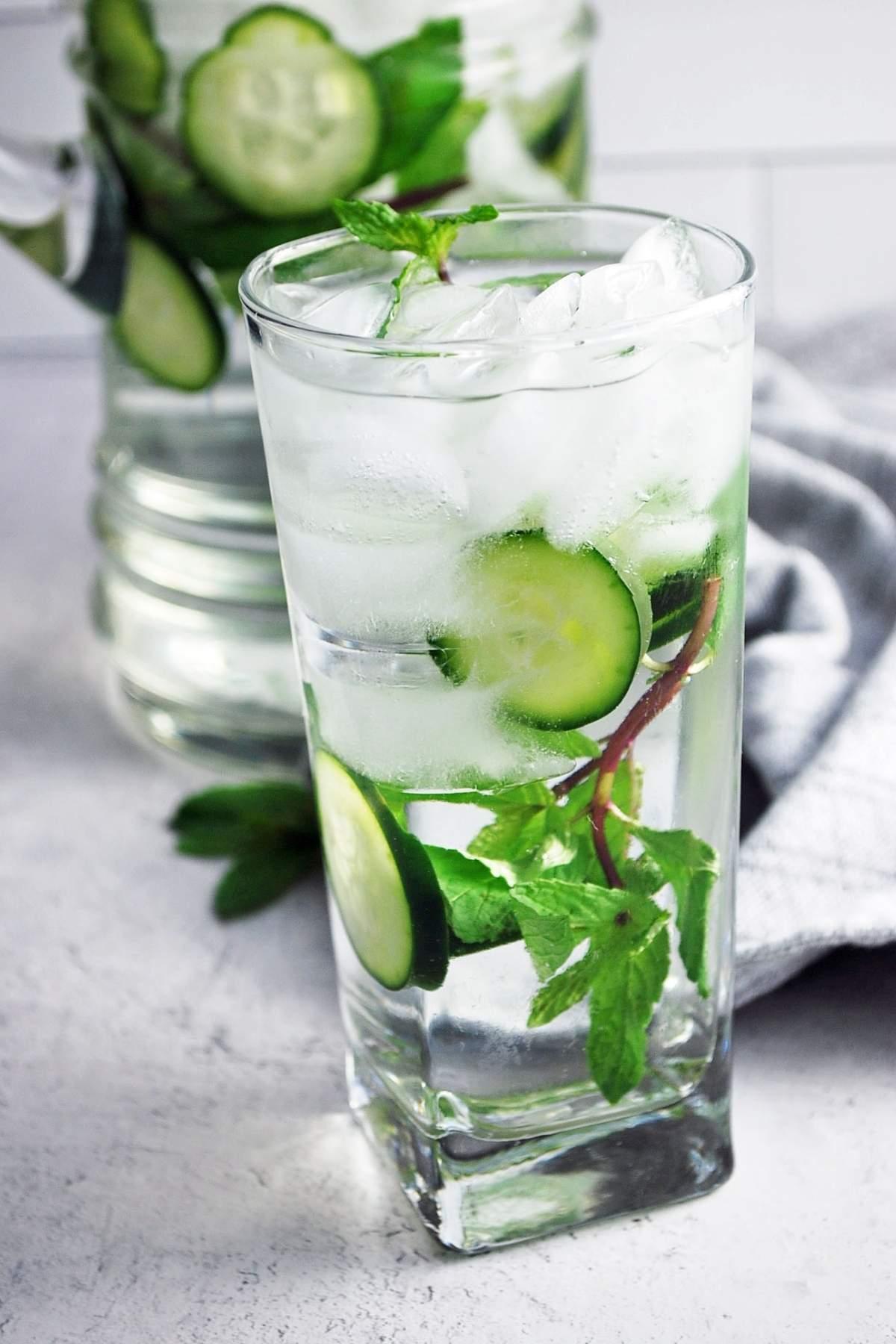 glass of cucumber mint infused water with ice cubes and fresh cucumber and mint sprigs