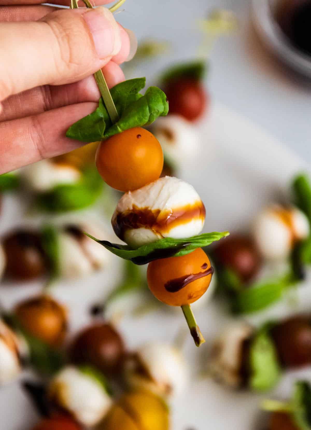 hands holding a plate of caprese skewers