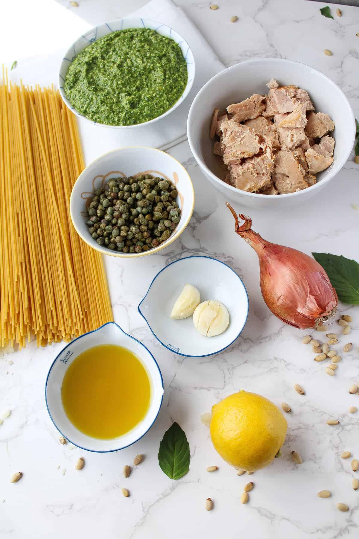 ingredients for pesto pasta with artichoke hearts and capers laid out on a wooden table