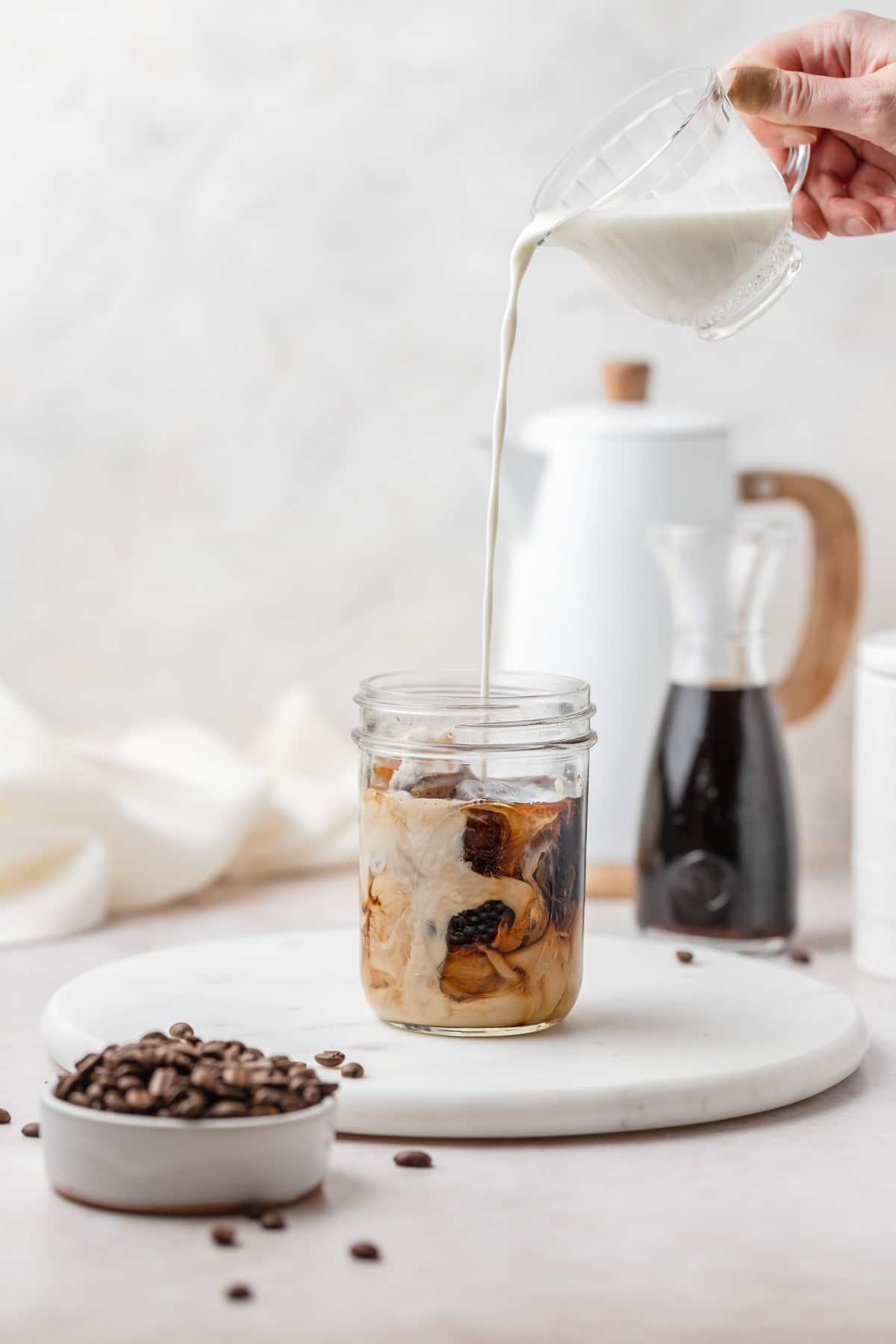 glass of vanilla bean cold brew with vanilla beans and coffee beans