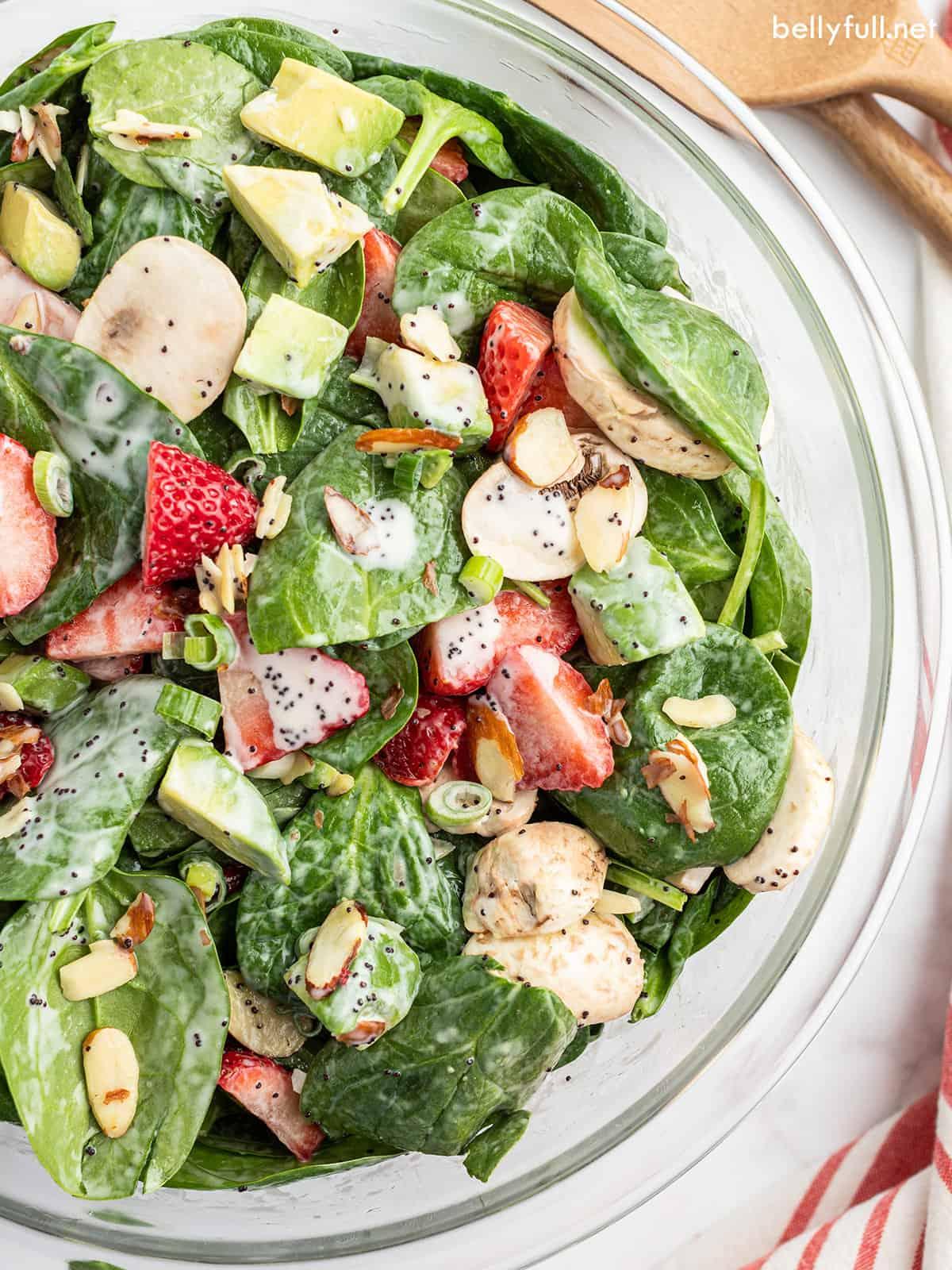 close-up of strawberry spinach salad with poppy seed dressing being tossed