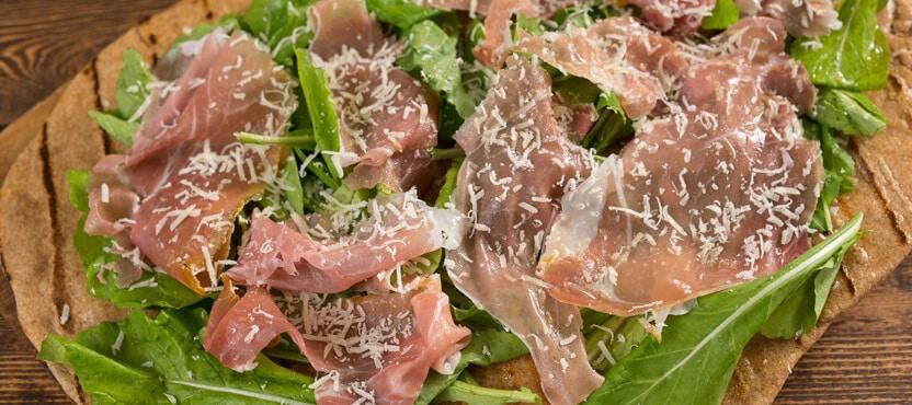 Finished grilled pizza with prosciutto and arugula being sliced