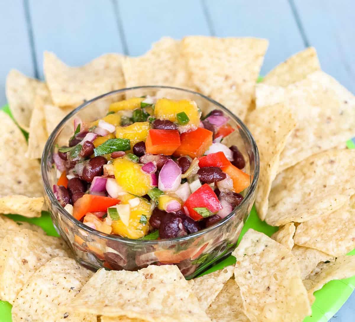 vibrant mango salsa in a glass bowl, surrounded by colorful tortilla chips and cilantro