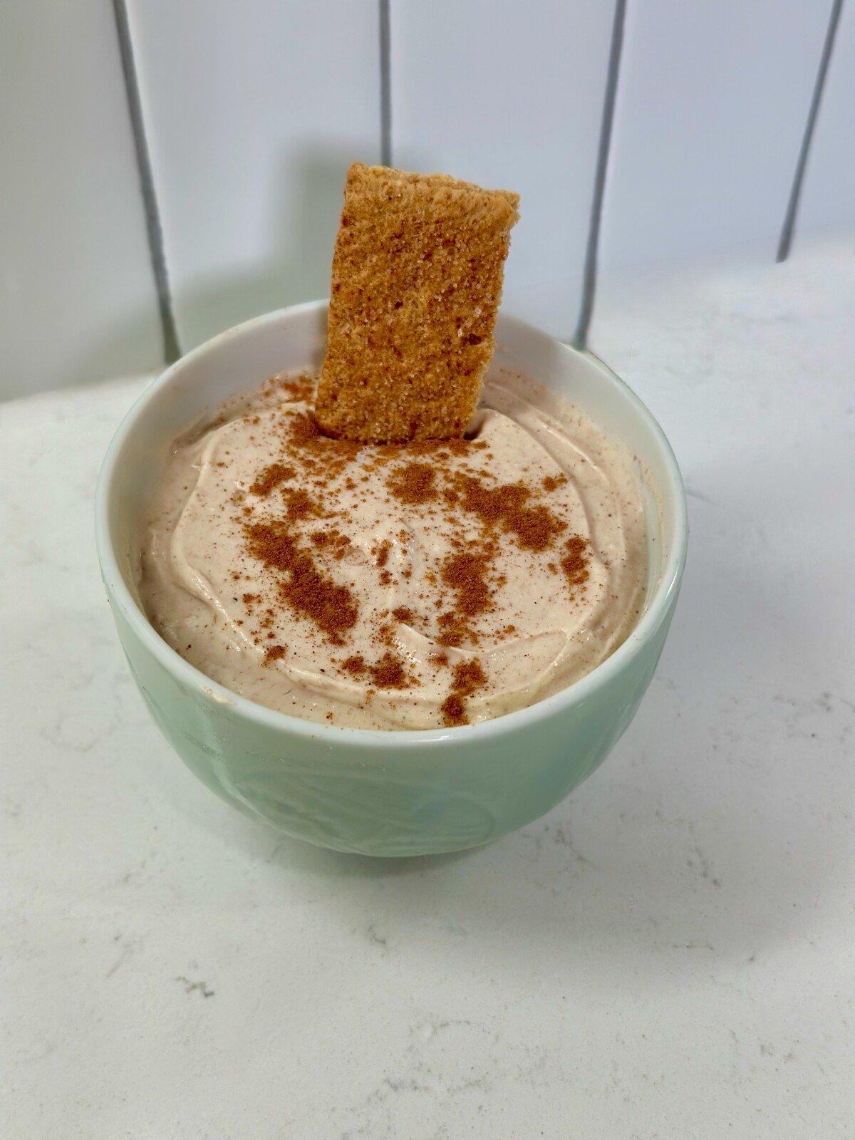 snickerdoodle cheesecake dip in a bowl with cinnamon sticks and graham crackers