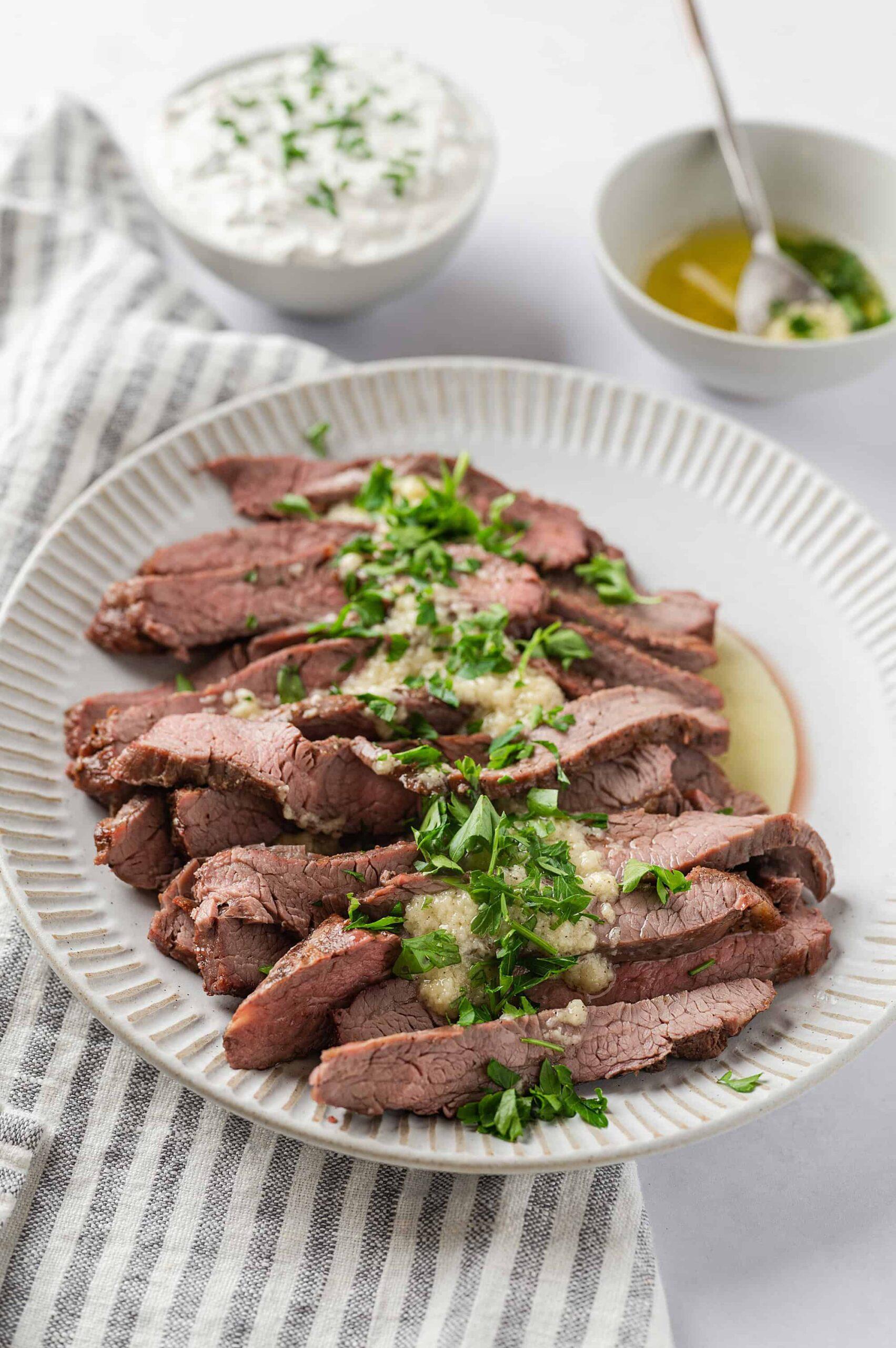 sliced garlic parmesan flank steak on a plate, garnished with parsley