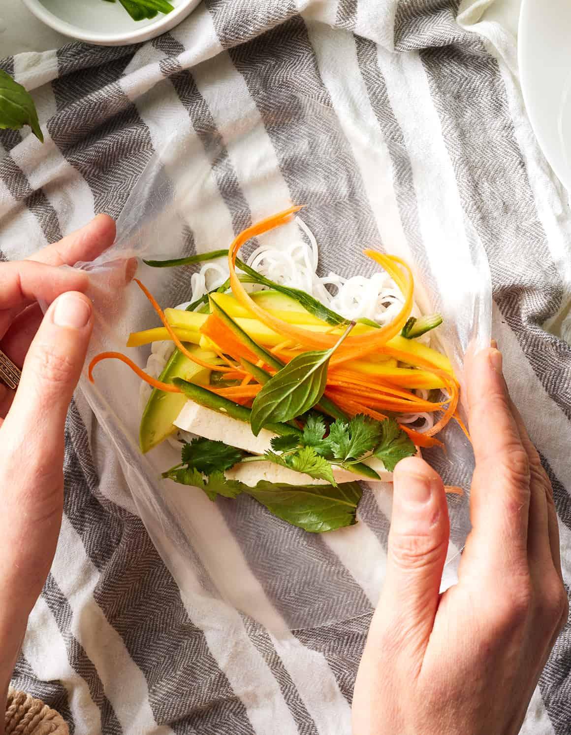 hands wrapping asian slaw spring rolls on a kitchen counter