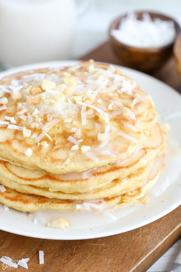 a stack of coconut cottage cheese pancakes drizzled with syrup and sprinkled with toasted coconut flakes