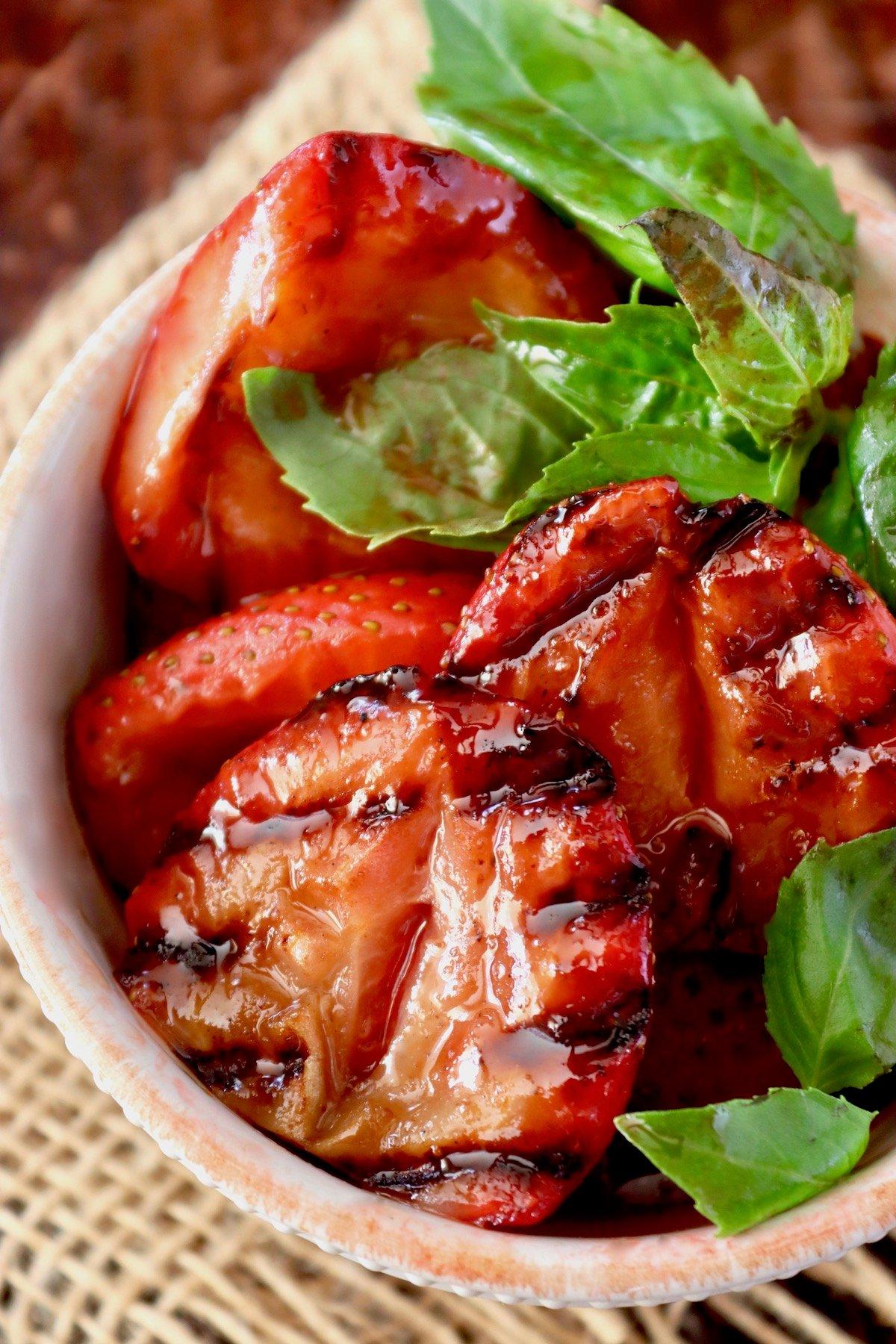 close-up shot of strawberry glazed ribs on a grill, garnished with fresh strawberries and basil