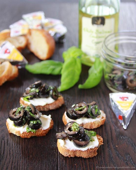 close-up of a hand spreading olive tapenade on a crostini