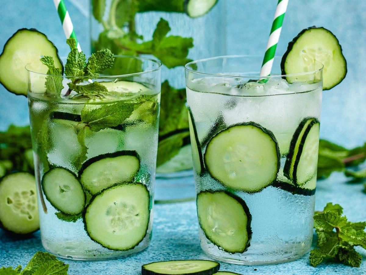several glasses of cucumber mint water garnished with cucumber slices and mint sprigs on a table