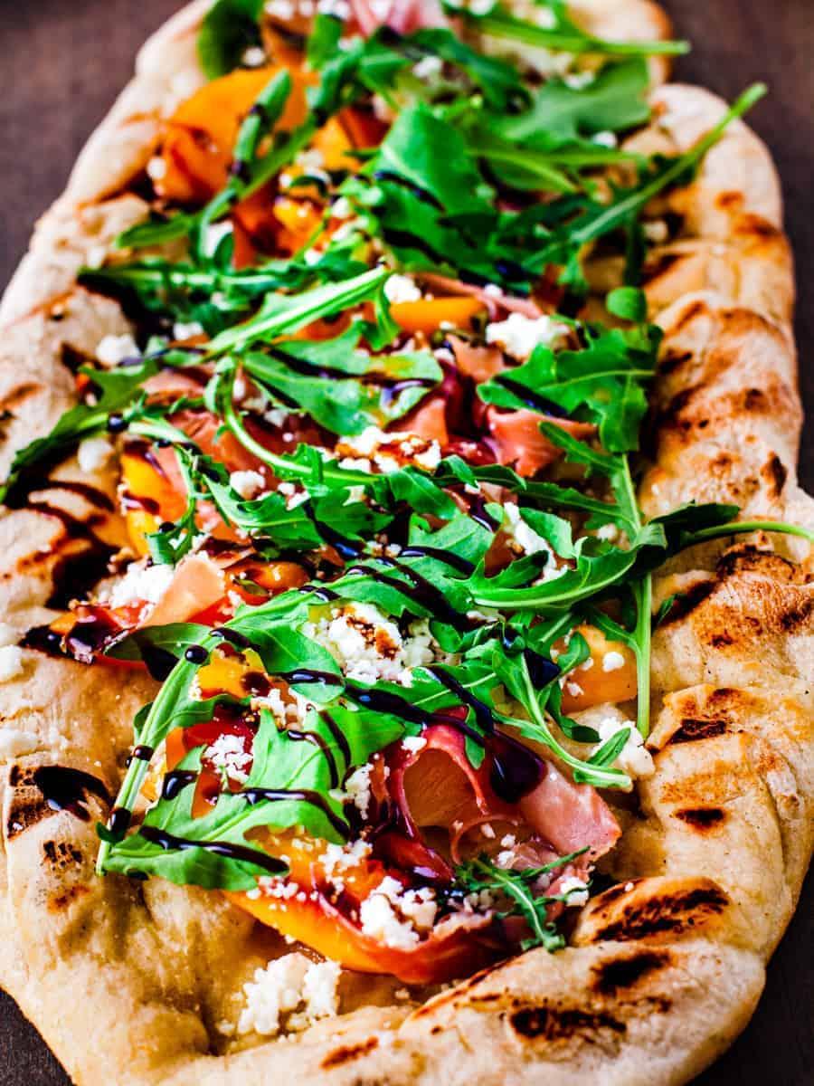 close up of grilled peach prosciutto pizza with balsamic glaze