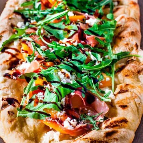 close up of grilled pizza being assembled with prosciutto arugula and balsamic