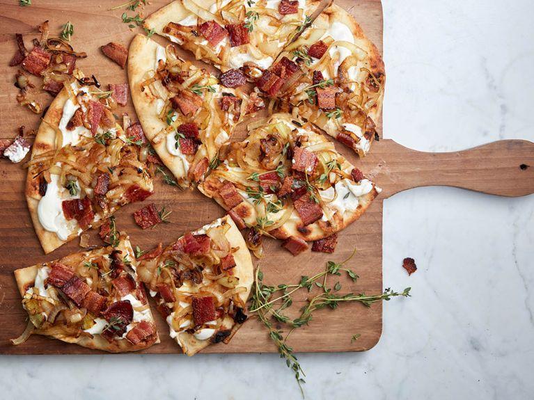 Slices of bacon and caramelized onion pizza being served on a wooden board