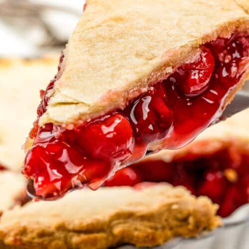a hand serving a slice of clean eating cherry pie