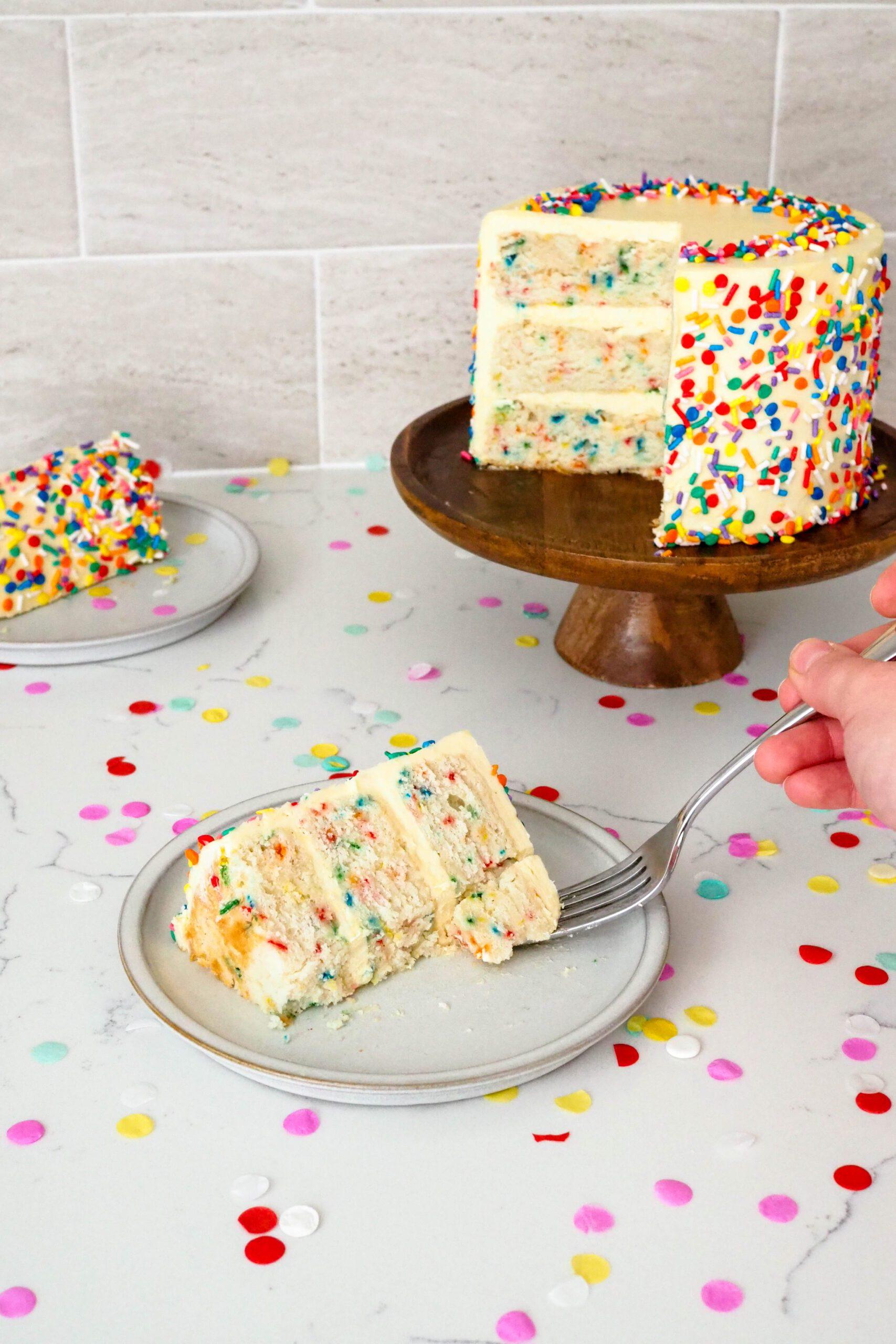 hands assembling a confetti vanilla layer cake