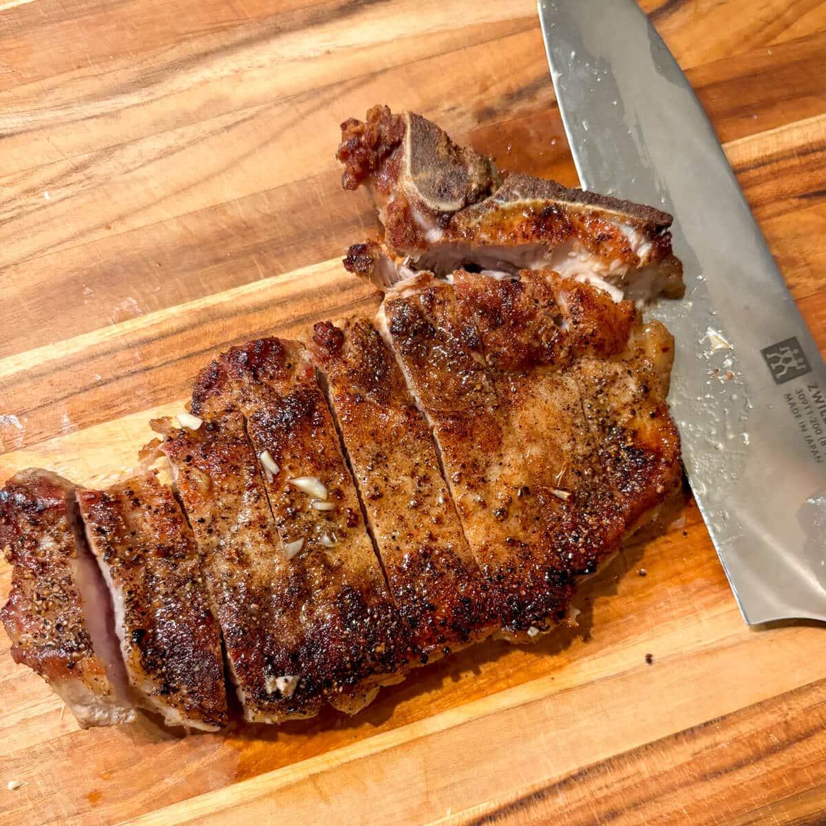 Cooked black garlic pork chops resting on a cutting board, ready to be served.