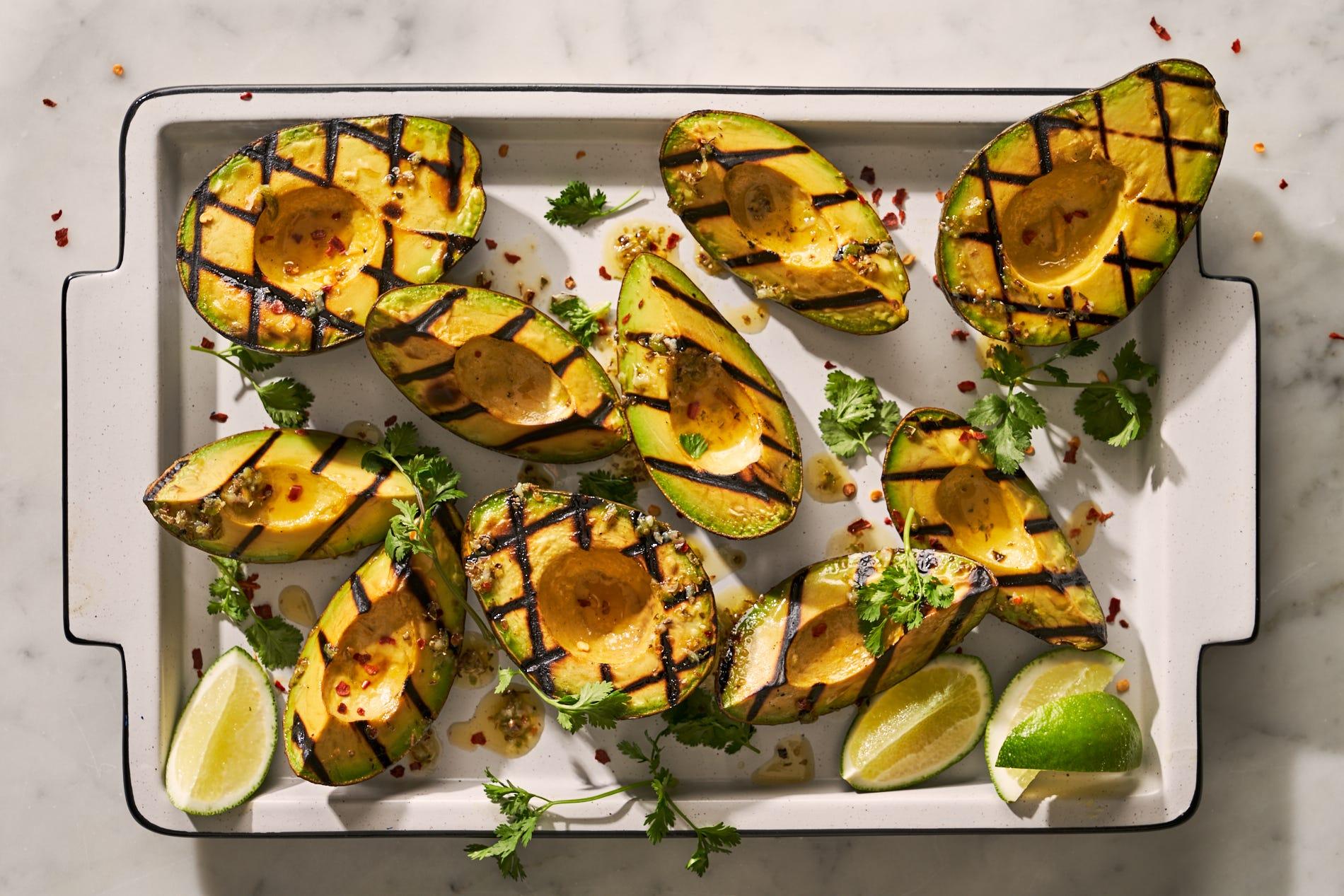 overhead shot of a platter of grilled avocado with lime wedges and cilantro sprigs