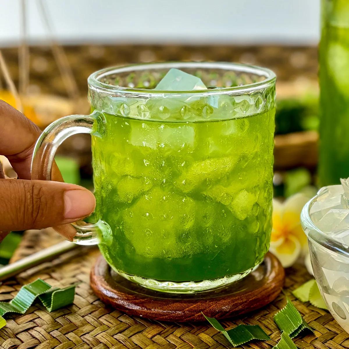 a pitcher filled with rosewater pandan punch surrounded by fresh ingredients like pandan leaves and roses