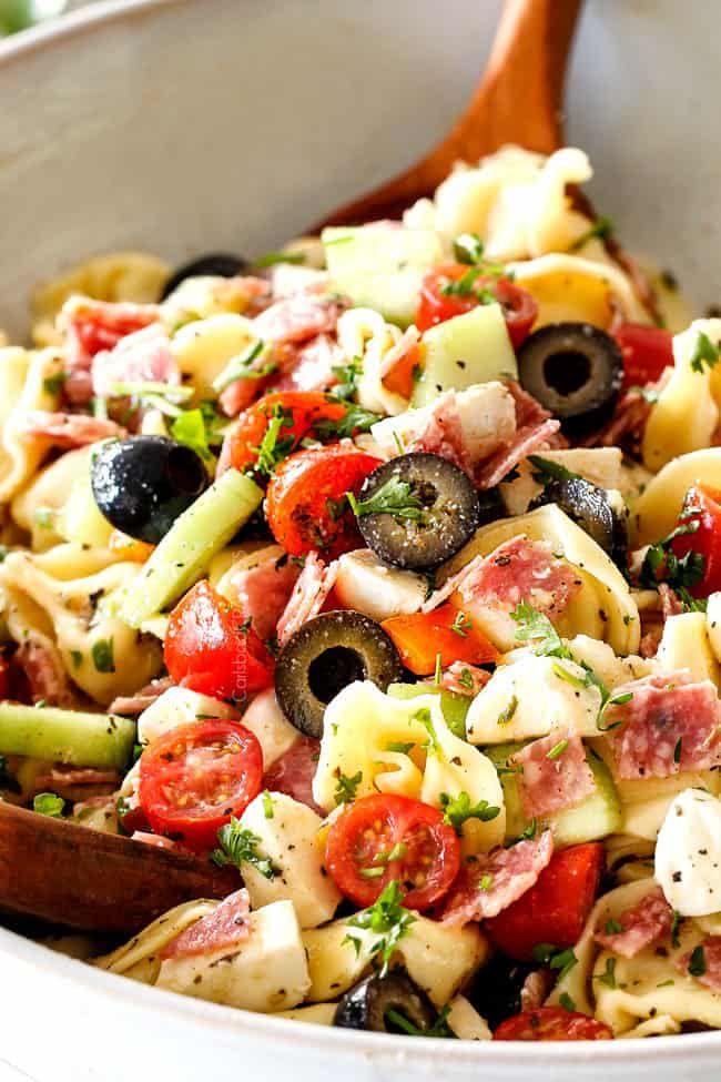 pasta salad being tossed in a bowl with dressing