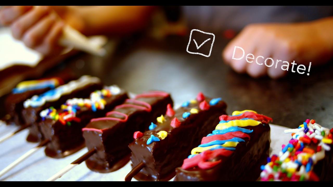 A group of people, including children, decorating brownie pops with sprinkles