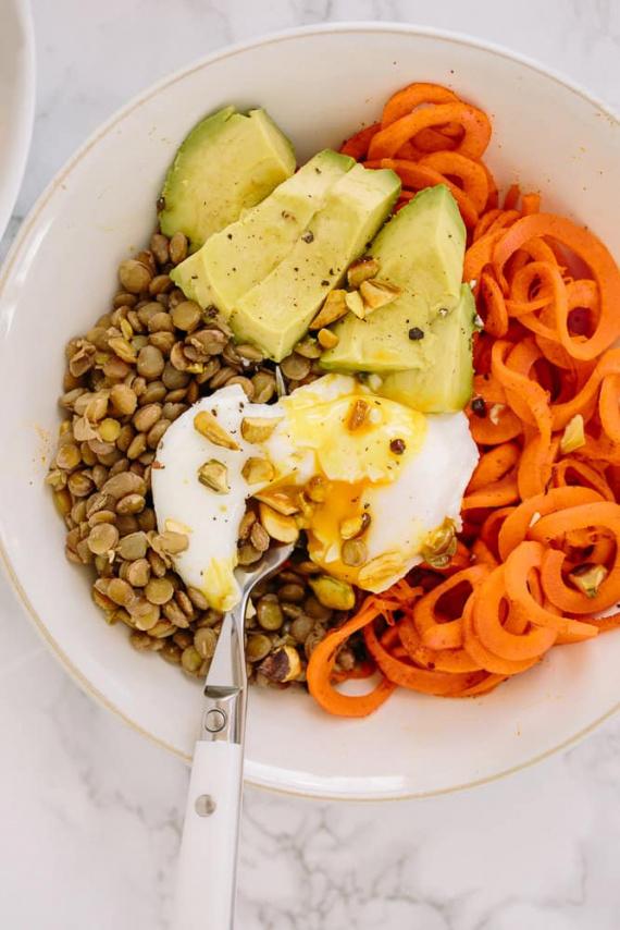 close-up of a lentil and carrot protein bowl with various toppings like avocado, cilantro, and a lime wedge