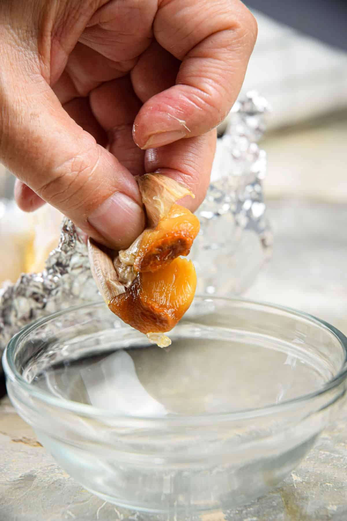 close-up of roasted garlic cloves being squeezed into a bowl