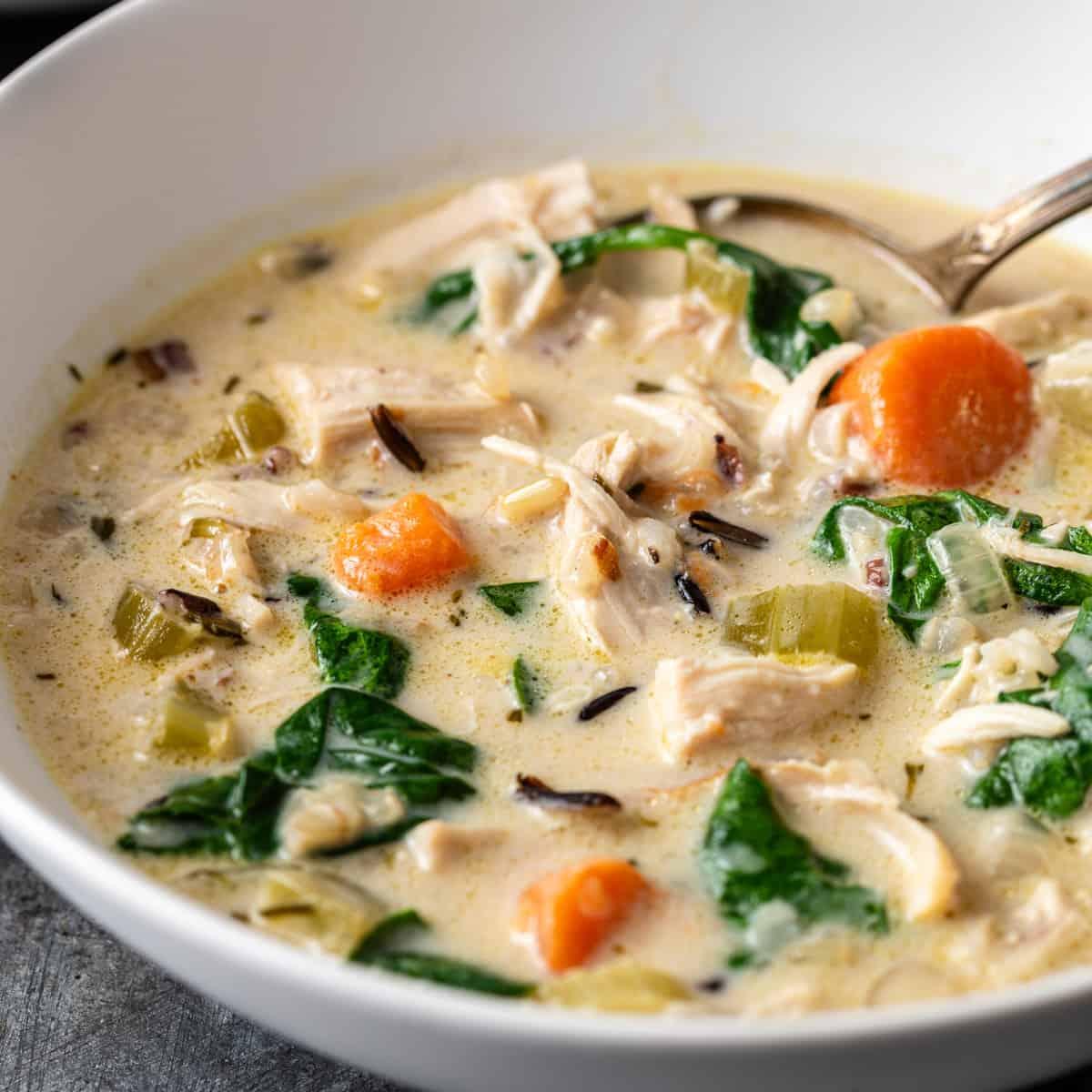 A bowl of chicken and wild rice soup with various vegetables such as carrots, celery, and spinach