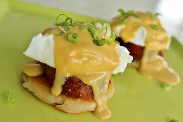 close up of a pork and bacon benedict with hollandaise sauce dripping