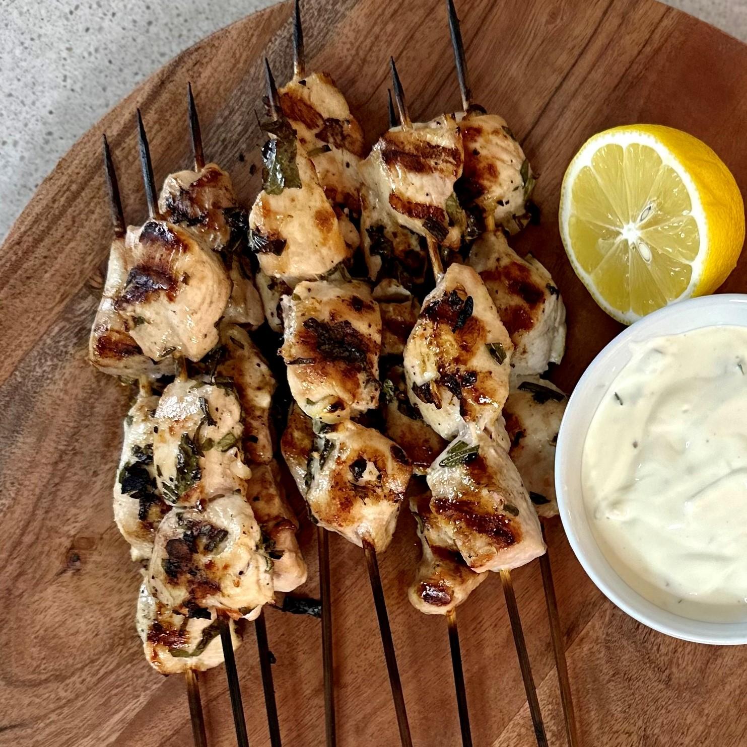 close up of the lemon herb marinade being poured over chicken skewers