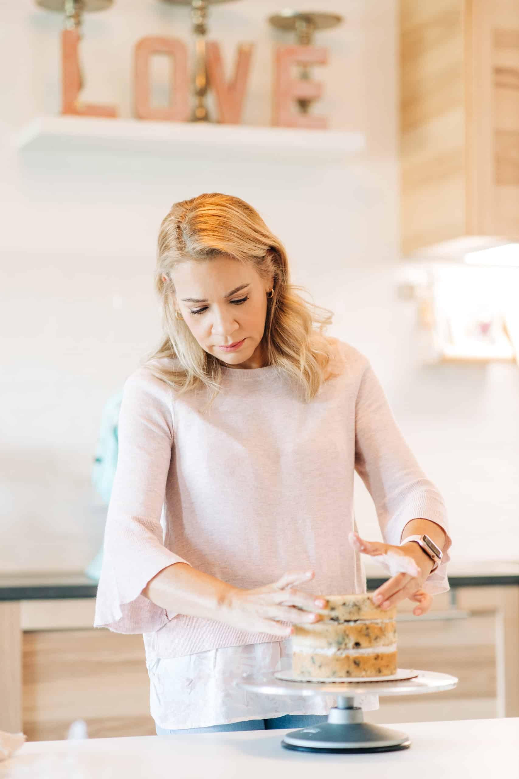 woman frosting a layered artisan cake in her kitchen