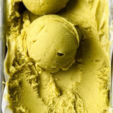 a person smiling while holding a cardamom pistachio ice cream sandwich outdoors