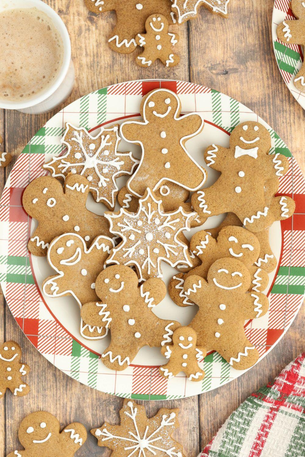 Close-up of beautifully decorated gingerbread cookies on a rustic wooden board, some with intricate white royal icing details, surrounded by festive holiday decor like cinnamon sticks and star anise