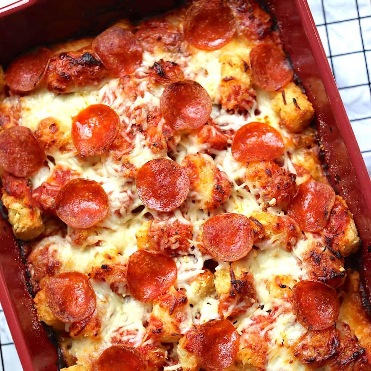 Close-up of a bubbling pizza tot casserole, golden brown tater tots, melted cheese, pepperoni slices, and a vibrant tomato sauce, ready to serve