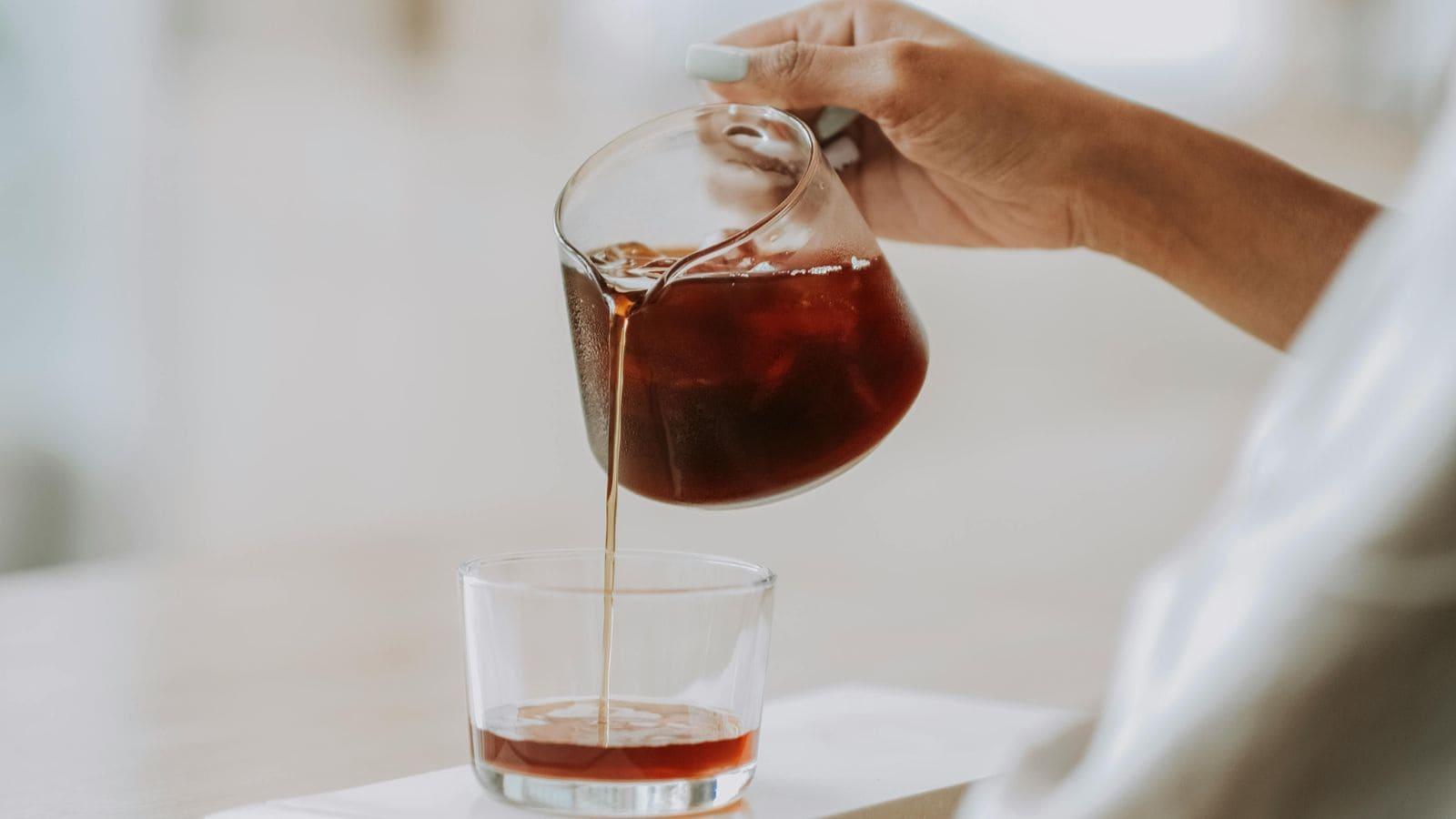 a person pouring cold brew coffee over ice into a clear glass