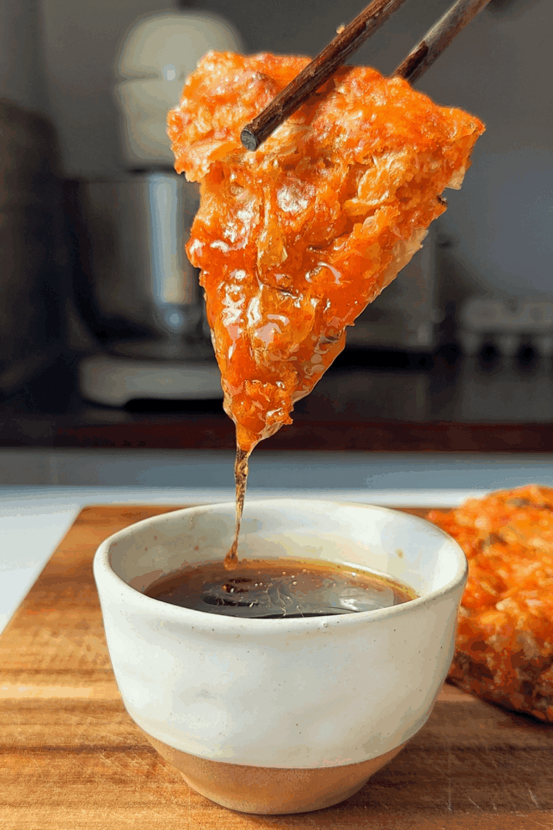 A hand dipping a kimchi cake pop into a glaze