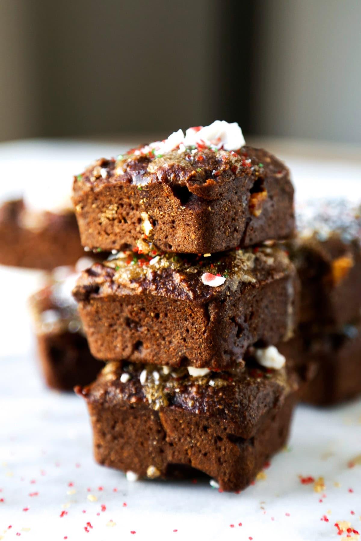 a hand holding a vegan tofu brownie with chocolate chips, with a blurred background of a kitchen