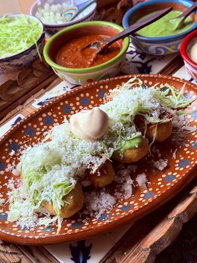 A plate of molotes quesadillas garnished with salsa, avocado, and crema