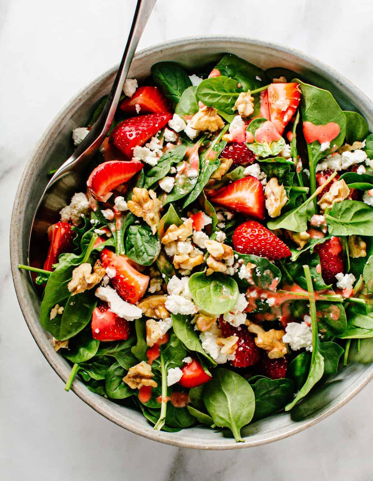 person tossing strawberry spinach walnut salad