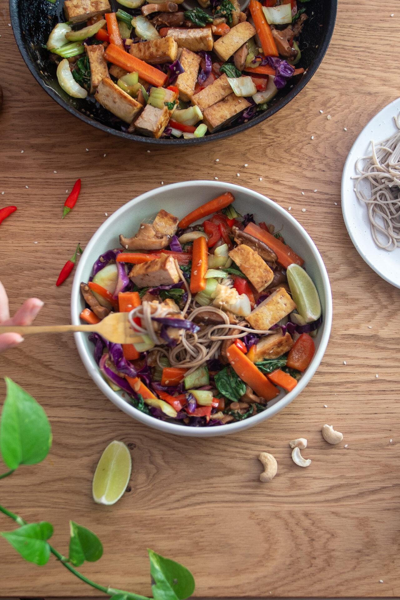 overhead view of a colorful cardamom tofu stir-fry in a serving bowl, garnished with sesame seeds and fresh herbs