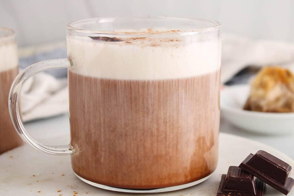 close up shot of a frothy flax seed chai latte being poured into a glass