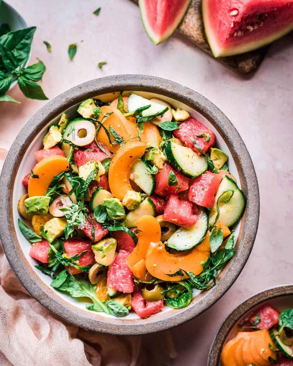 Overhead view of the Hawaiian watermelon cucumber pasta salad in a large serving bowl surrounded by tropical decorations