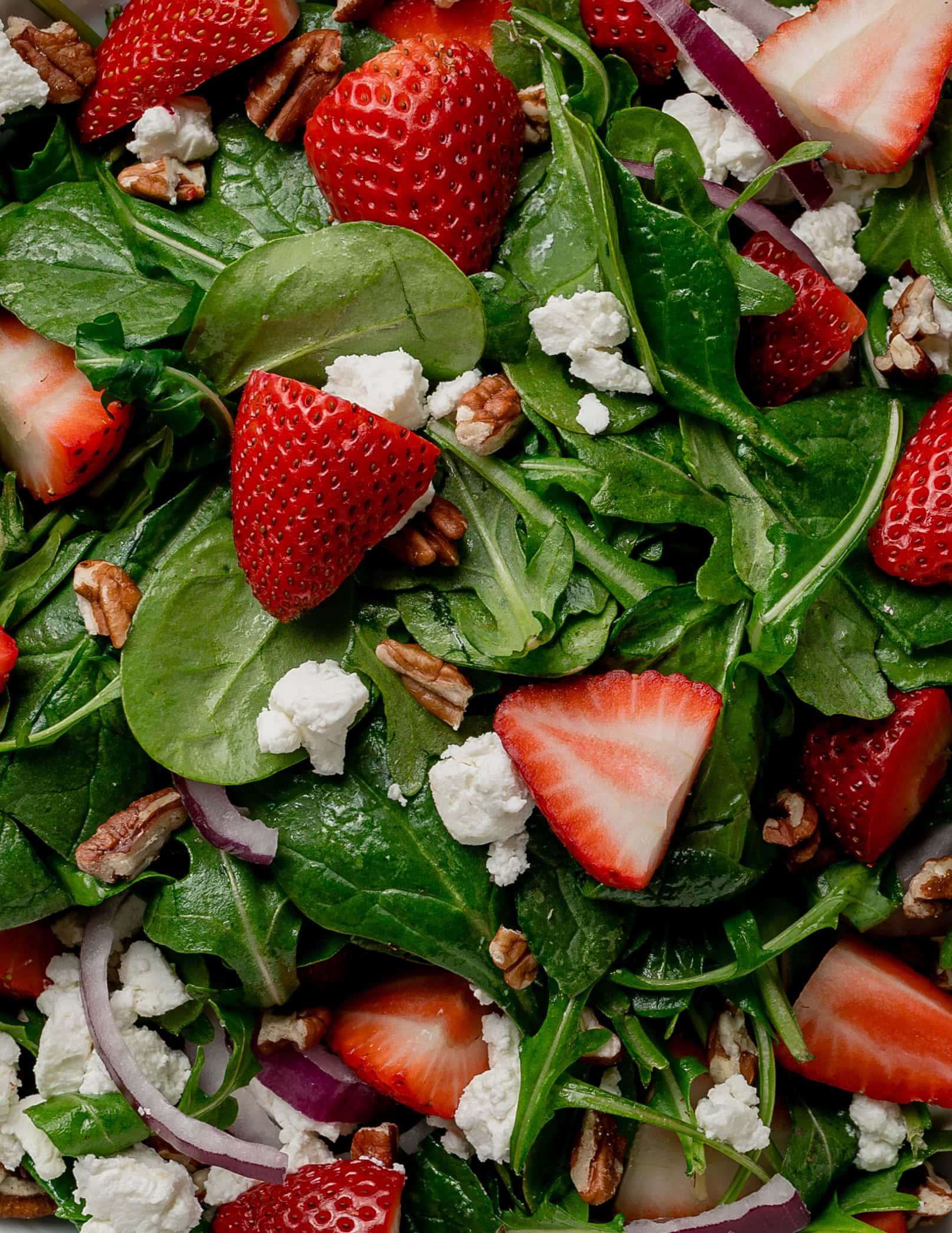 close-up of strawberry spinach salad with arugula being tossed