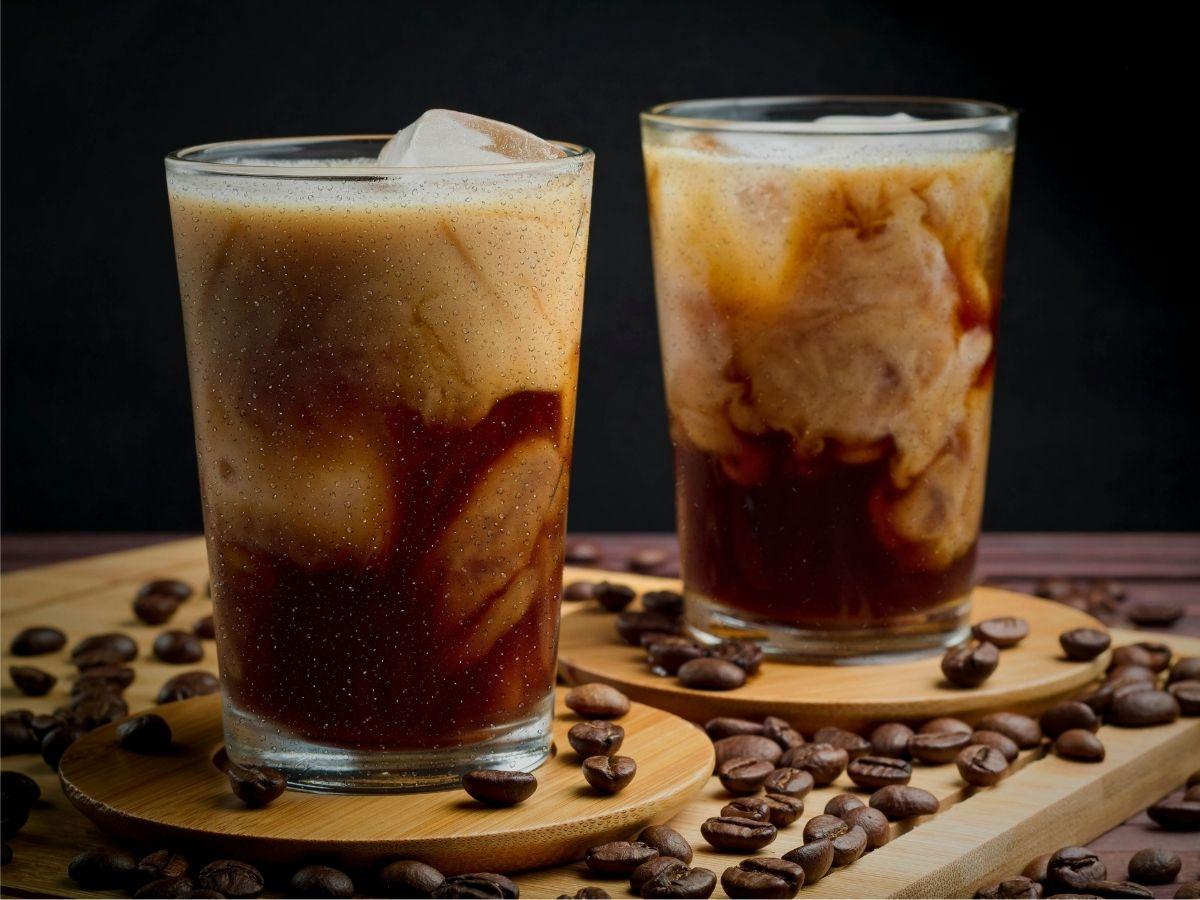two glasses of cold brew iced coffee, one with cream or milk swirling in, outdoor setting