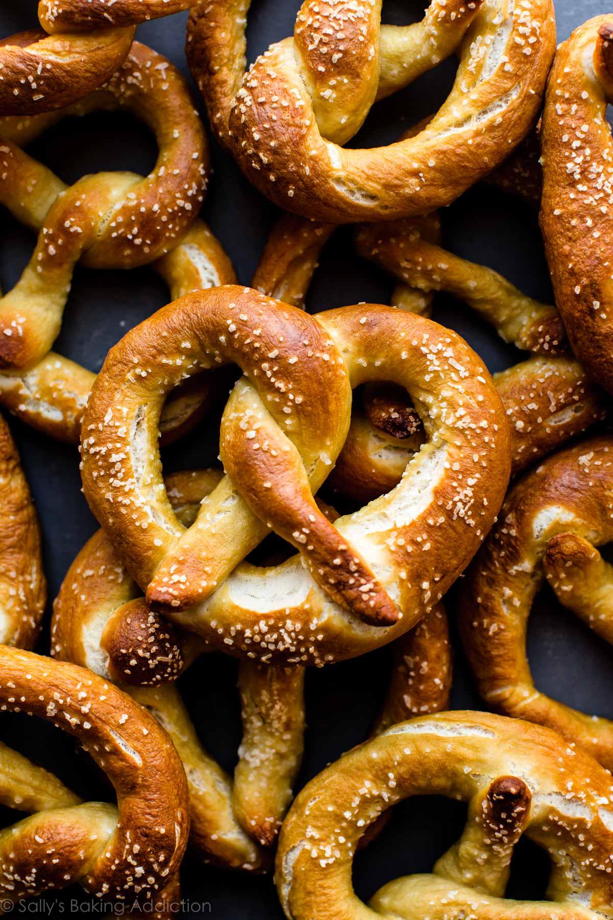 Hand twisting soft pretzel dough on a wooden board, close-up of golden-brown buttered pretzel with coarse salt.