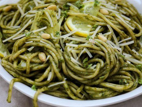 close up of pesto pasta with artichoke hearts and capers being tossed in a bowl