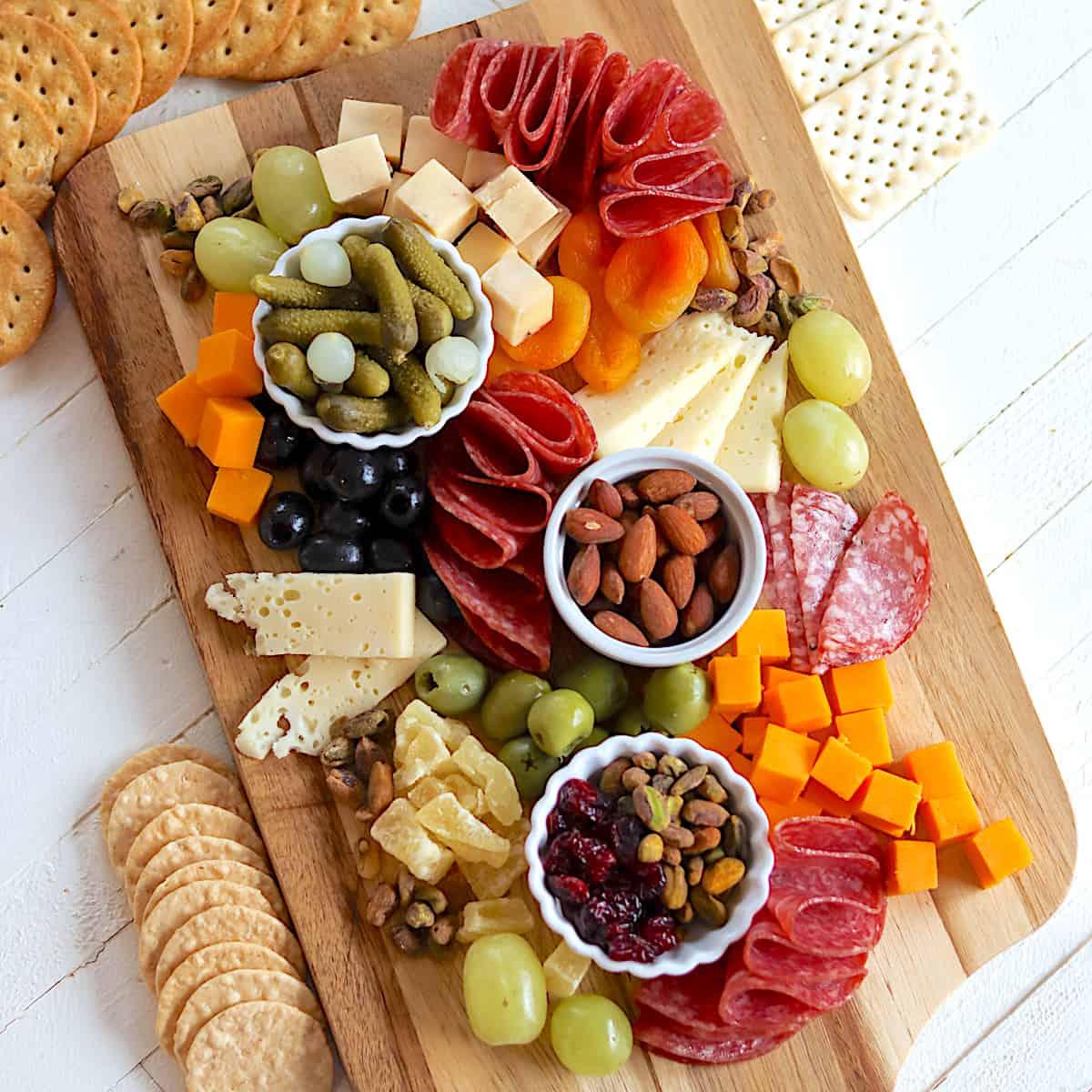 a variety of cheeses, nuts, and fruits arranged around dried mango on a charcuterie board