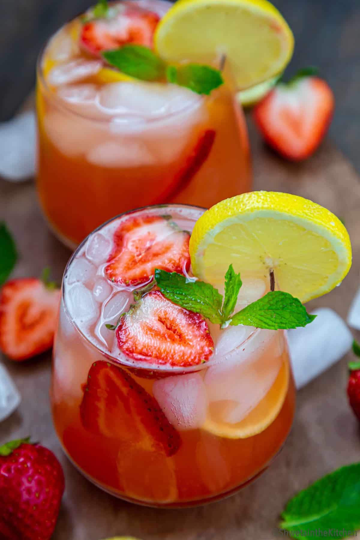 two glasses of strawberry lemonade spritzer with ice, garnished with strawberries and lemon slices
