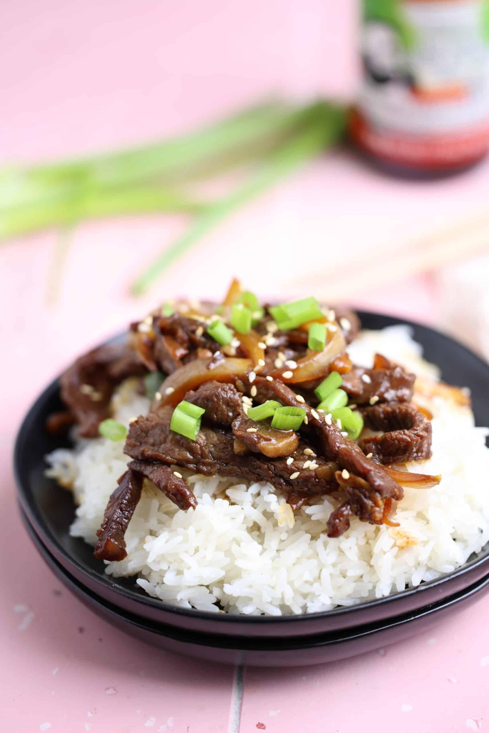 plated beef and bell pepper stir-fry with rice, garnished with sesame seeds and green onions