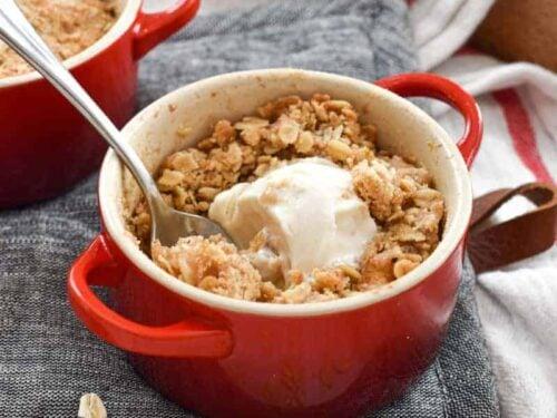 side view of a spoonful of apple crisp being lifted from a ramekin, showing the layers of apple and crumble topping